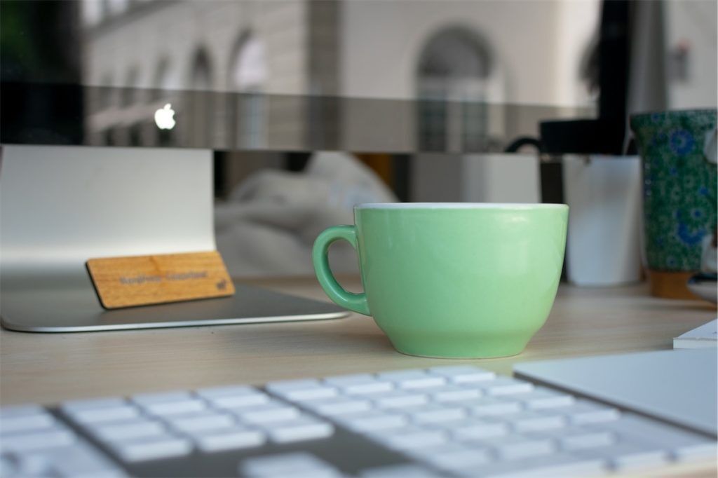 Eine grüne Kaffeetasse vor dem Bildschirm eines iMacs.